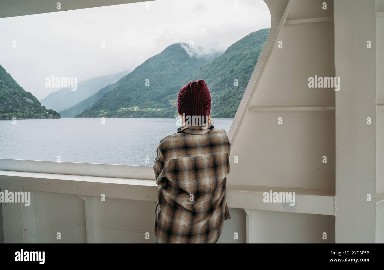 Femme profitant des paysages de fjord sur le ferry norvégien avec des montagnes vertes brumeuses en arrière-plan. Scène capture l'essence d'un voyage détendu, exploration dans Banque D'Images