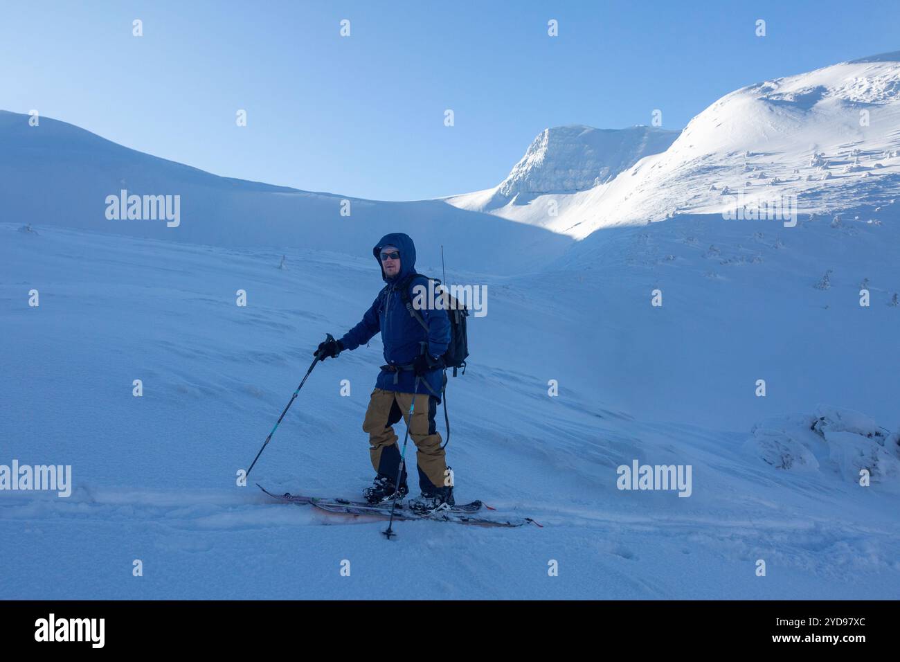Un moment de solitude : un skieur profite de la beauté paisible d'un paysage hivernal, le soleil projetant des ombres dramatiques sur la montagne. Banque D'Images