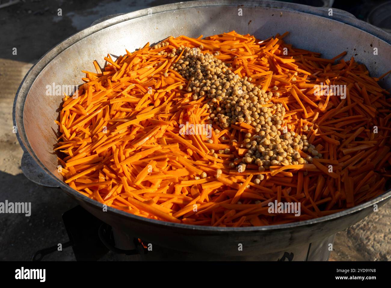 Cuisson du pilaf dans un grand chaudron, avec des carottes et des pois chiches jetés dans la casserole avec de l'huile pour la friture. Banque D'Images