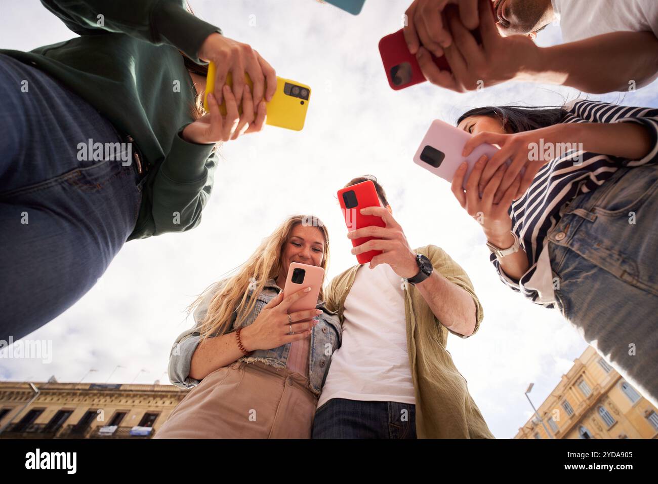 Vue d'en bas du groupe de jeunes gens debout en cercle tenant des téléphones portables colorés Banque D'Images