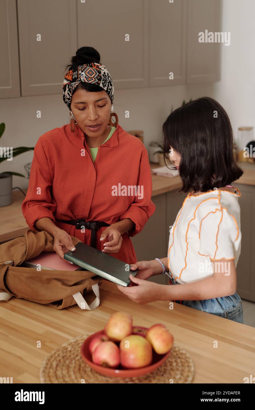 Deux femmes debout près du comptoir en bois engageant la conversation tout en tenant des livres. Bol de fruits avec des pommes ajoutant une touche de la maison dans l'espace de cuisine chaleureux Banque D'Images