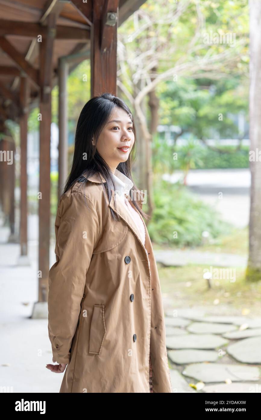 Une taïwanaise aux cheveux longs dans la vingtaine portant un trench beige passe son après-midi d'hiver sous les avant-toiTS dans le district de Xinyi, Taipei, Taiwan, on Banque D'Images