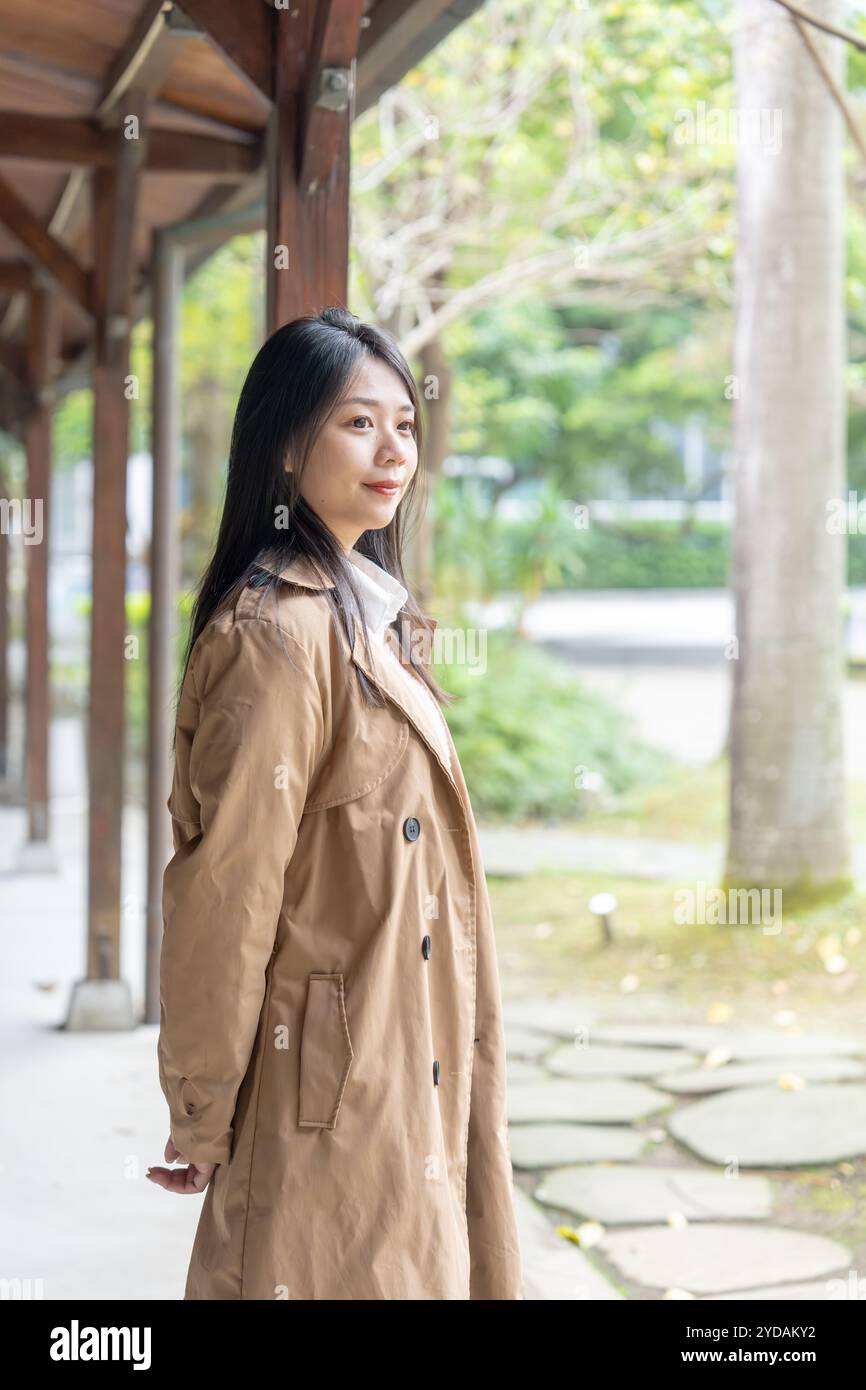 Une taïwanaise aux cheveux longs dans la vingtaine portant un trench beige passe son après-midi d'hiver sous les avant-toiTS dans le district de Xinyi, Taipei, Taiwan, on Banque D'Images