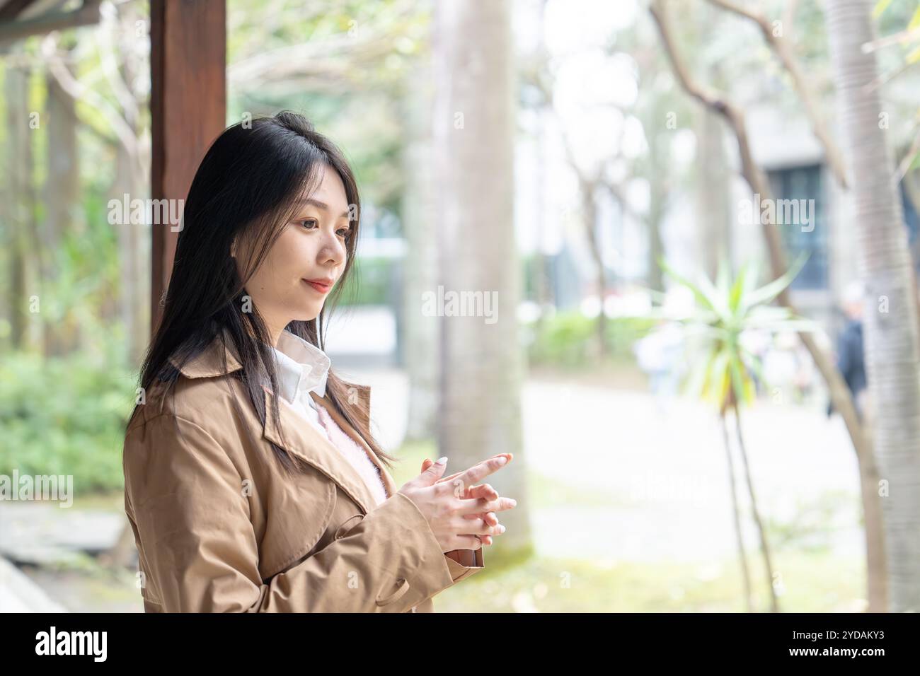Une taïwanaise aux cheveux longs dans la vingtaine portant un trench beige passe son après-midi d'hiver sous les avant-toiTS dans le district de Xinyi, Taipei, Taiwan, on Banque D'Images