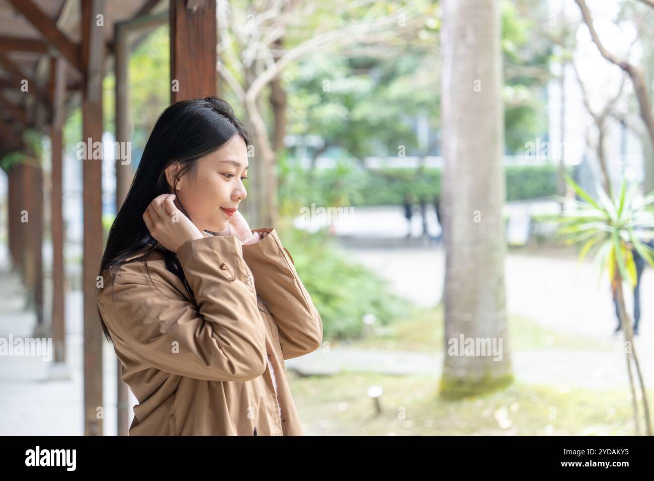 Une taïwanaise aux cheveux longs dans la vingtaine portant un trench beige passe son après-midi d'hiver sous les avant-toiTS dans le district de Xinyi, Taipei, Taiwan, on Banque D'Images