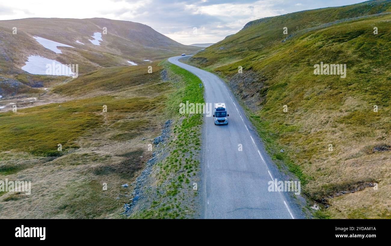 Un seul véhicule parcourt une route sinueuse à travers les superbes montagnes norvégiennes, avec des sommets enneigés et des pentes verdoyantes. North Cape ou Nordk Banque D'Images