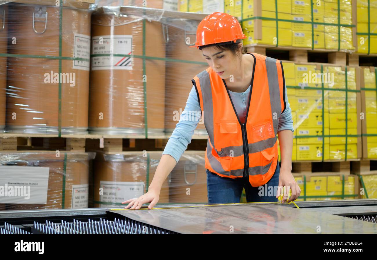 Une travailleuse mesure la taille d'une tôle d'acier découpée à partir d'un outil de coupe en acier. Banque D'Images