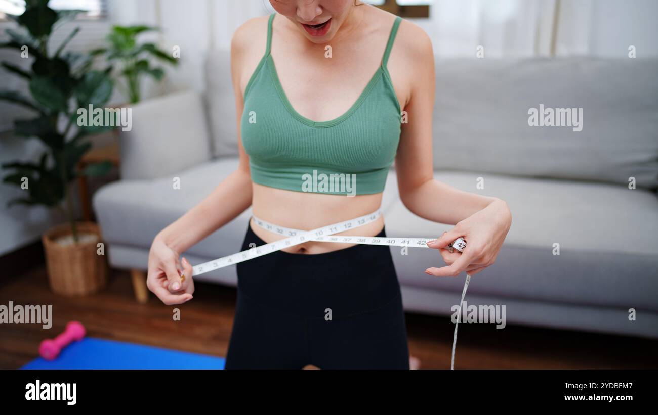 Femme mince utilisant le ruban à mesurer la taille à sa maison. Banque D'Images