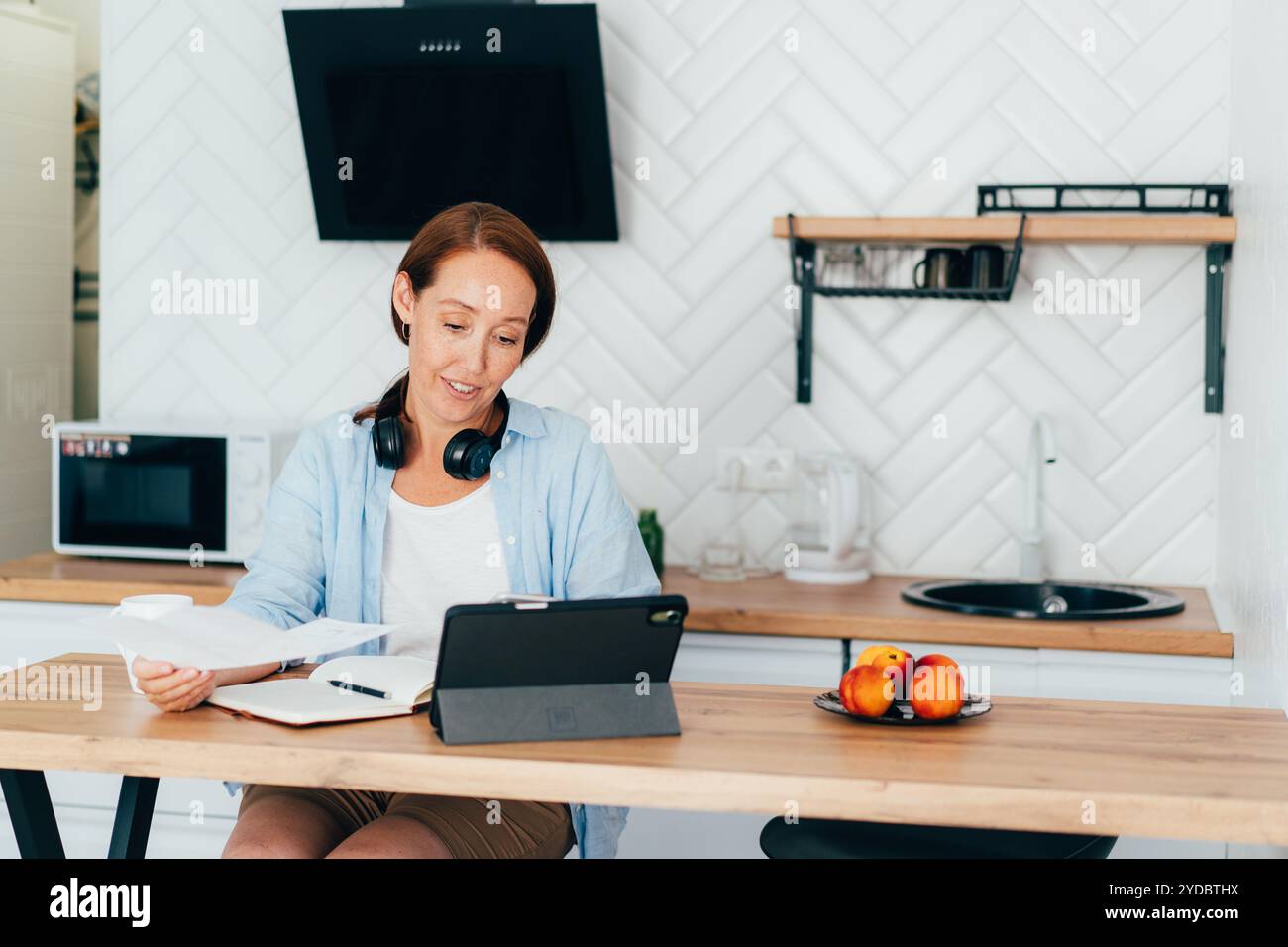 Une femme au foyer fait la comptabilité et la planification tout en étant assis à la table dans la cuisine avec une tablette d'ordinateur. Banque D'Images