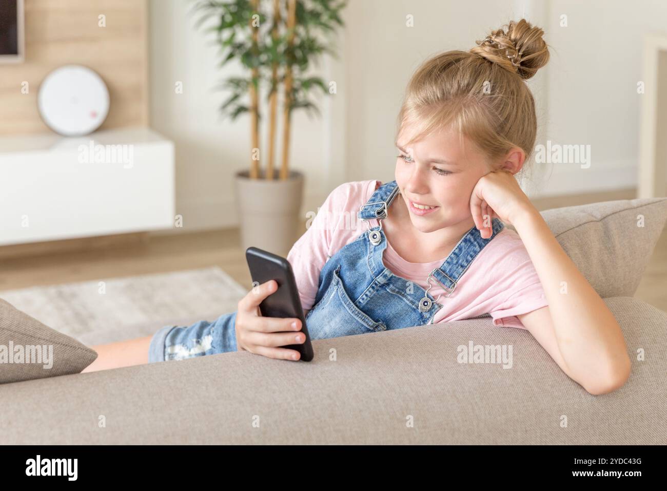 Petite fille jouant avec un téléphone portable à la maison sur un canapé Banque D'Images