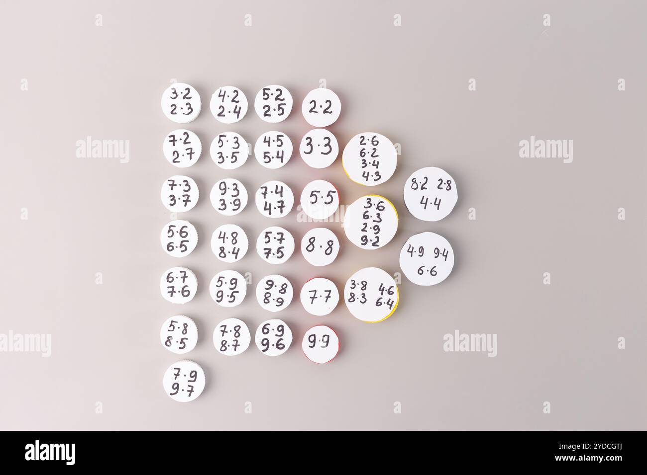 Bouchons de bouteilles en plastique avec tableaux de multiplication écrits à la main disposés en rangées sur un fond gris. Outil d'apprentissage mathématique DIY pour l'éducation des enfants et m Banque D'Images