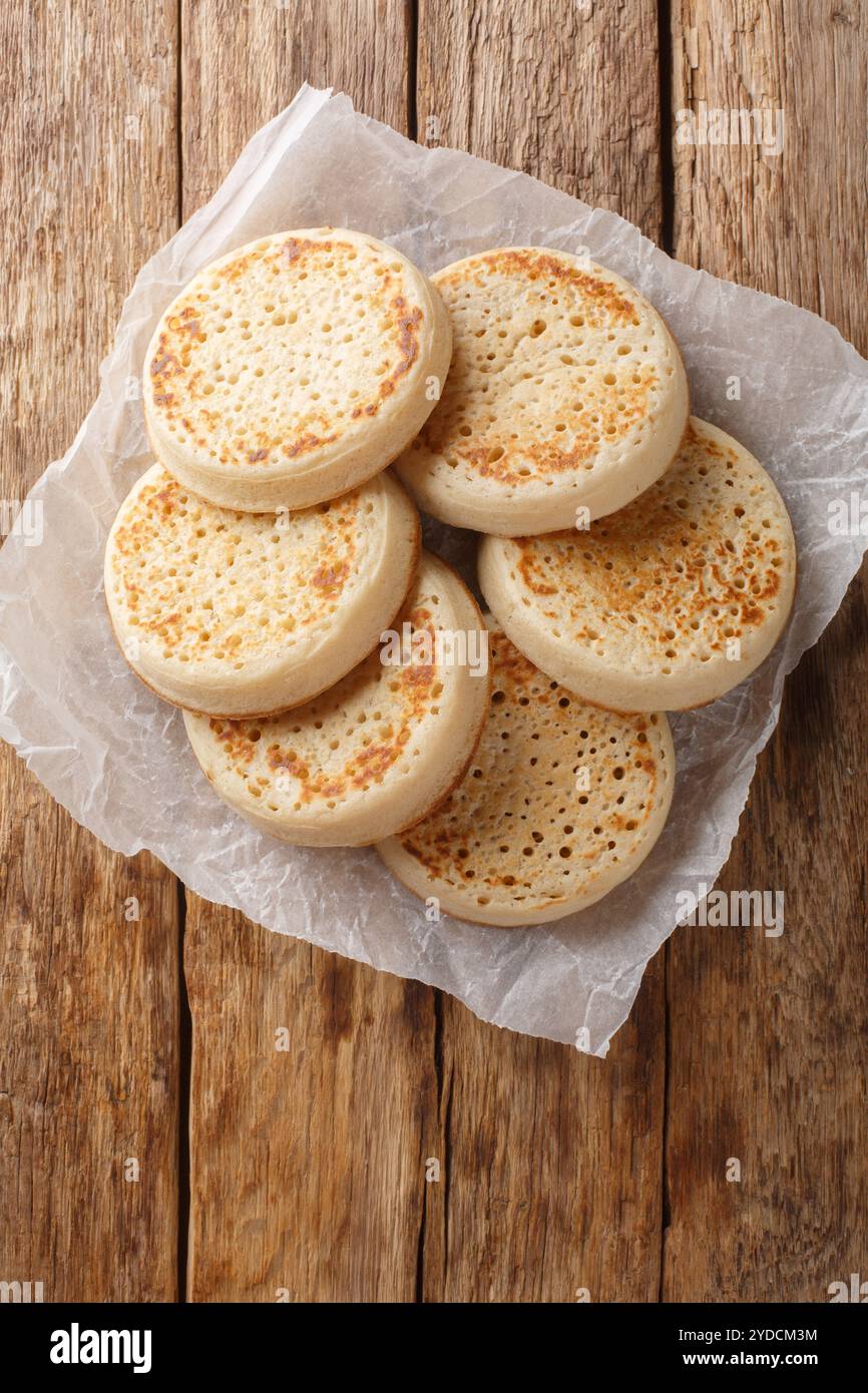 Gros plan de crumpets anglais fraîchement préparés sur du papier parchemin sur la table. Vue de dessus verticale Banque D'Images