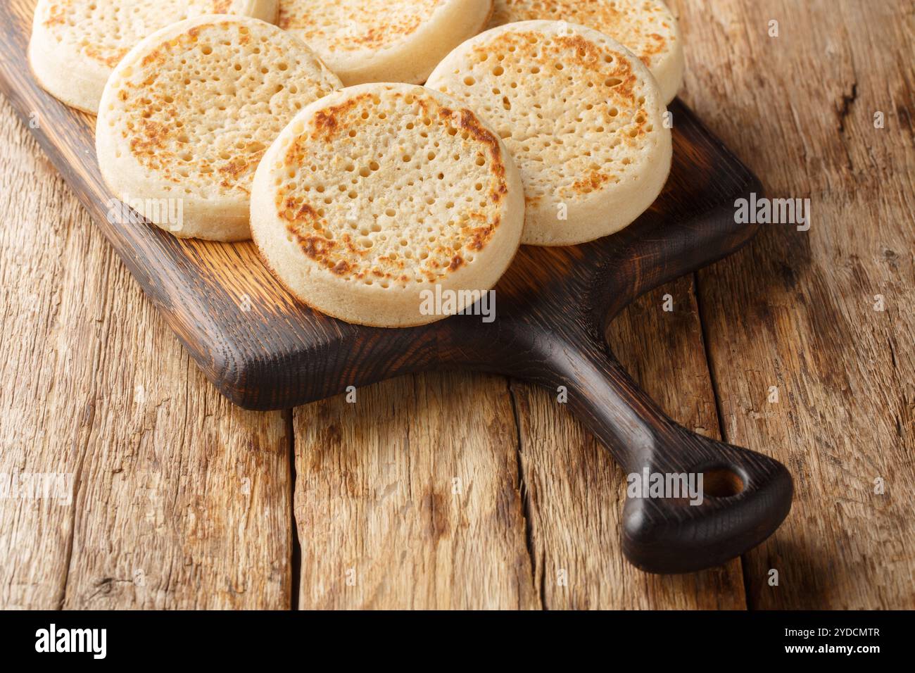 Gros plan de crumpets dorés frais sur la planche de bois sur la table. Horizontal Banque D'Images