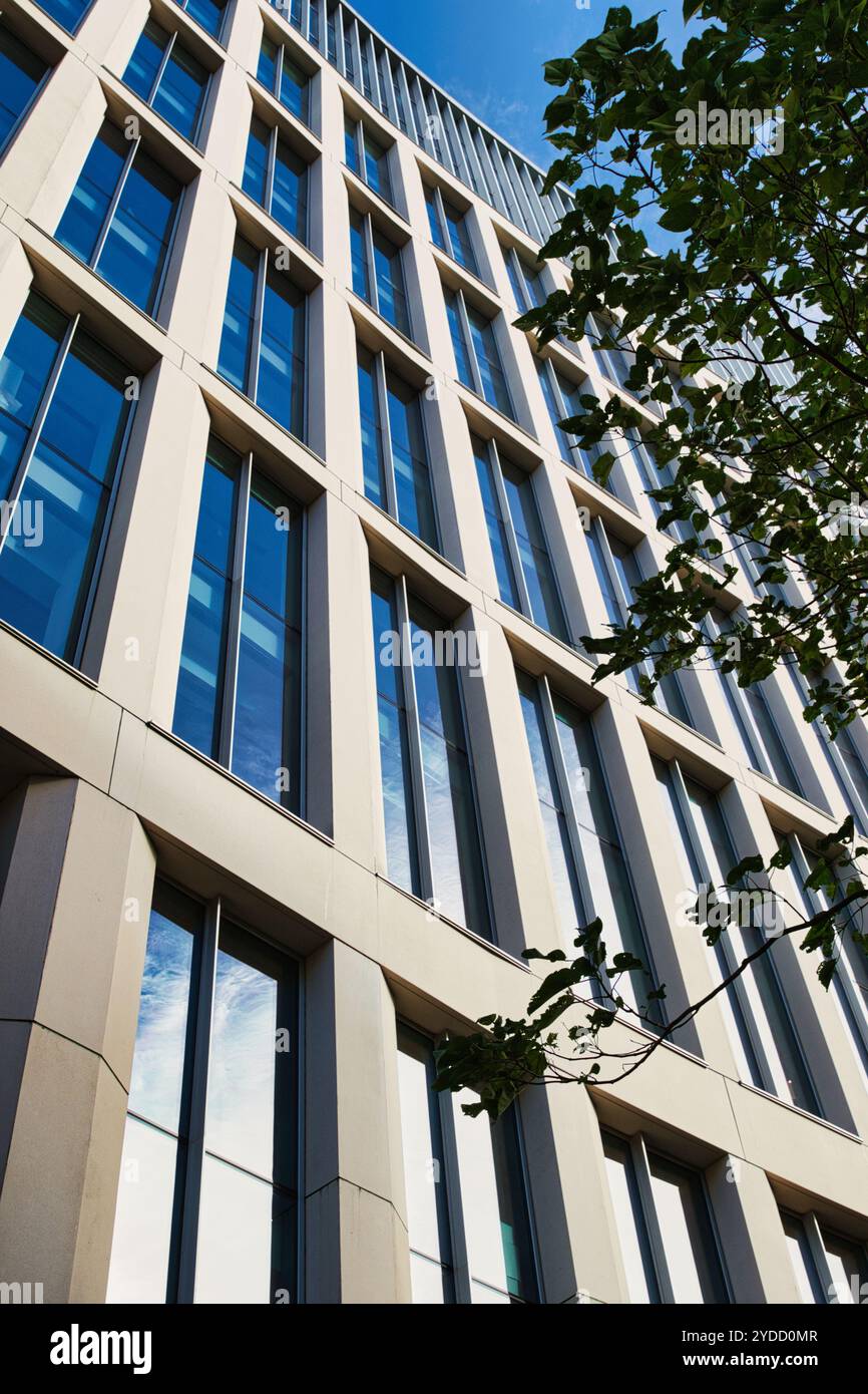 Une vue en angle bas d'un immeuble de bureaux moderne avec une façade beige clair, avec de nombreuses fenêtres et branches d'arbres au premier plan à Manchester, Banque D'Images