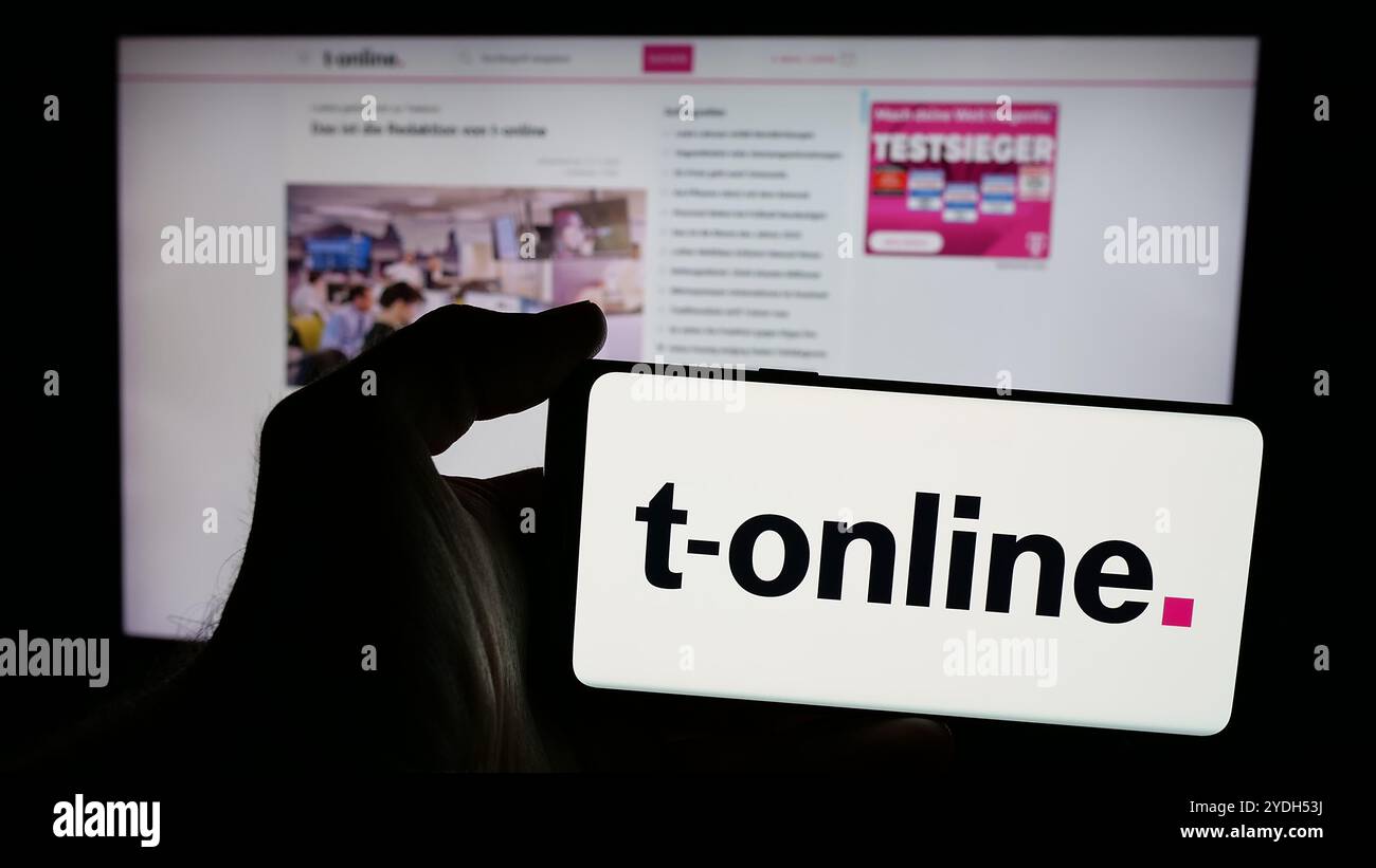 Personne tenant un smartphone avec le logo de la société allemande de médias en ligne t-online sur l'écran en face du site Web. Concentrez-vous sur l'affichage du téléphone. Banque D'Images