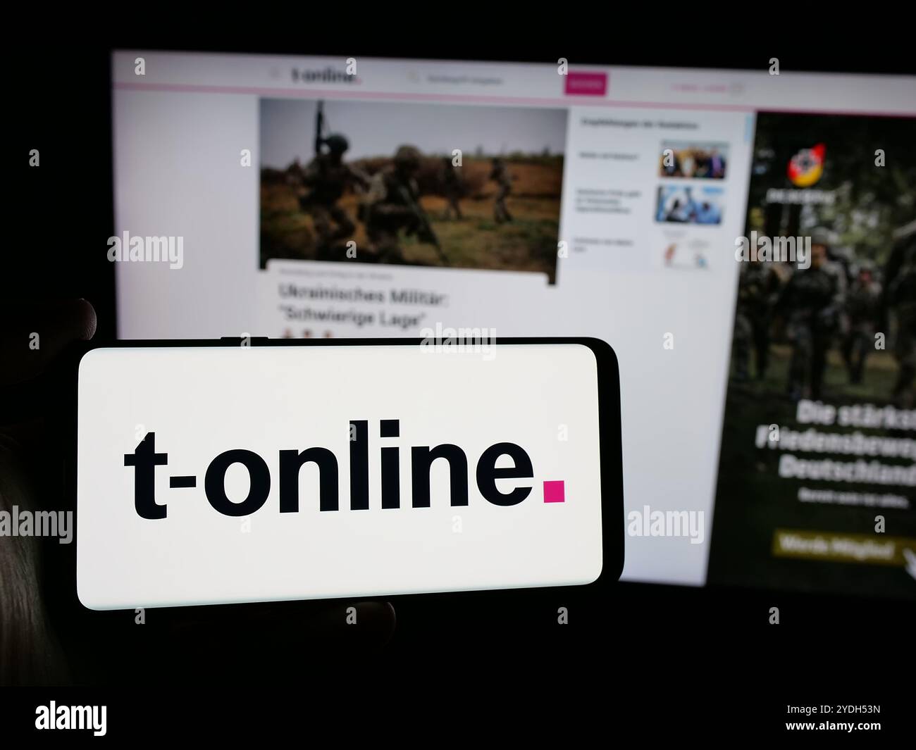 Personne tenant le téléphone portable avec le logo de la société allemande de médias en ligne t-online sur l'écran en face de la page Web de l'entreprise. Concentrez-vous sur l'affichage du téléphone. Banque D'Images
