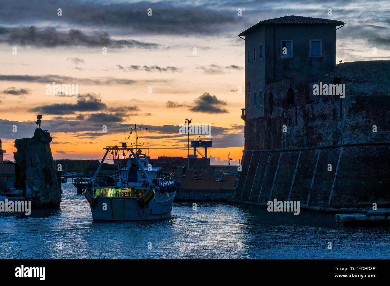Bateau sortant de Darsena Vecchia à Livourne au coucher du soleil, avec la silhouette des bâtiments historiques et le port en arrière-plan, Italie Banque D'Images
