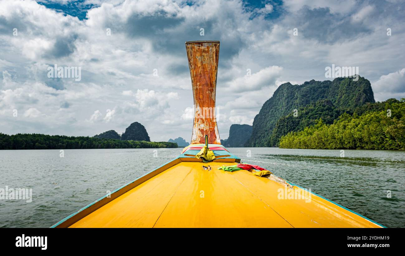 Vue de l'intérieur d'un bateau thaïlandais à longue queue jaune sur l'eau, entouré de collines verdoyantes Banque D'Images