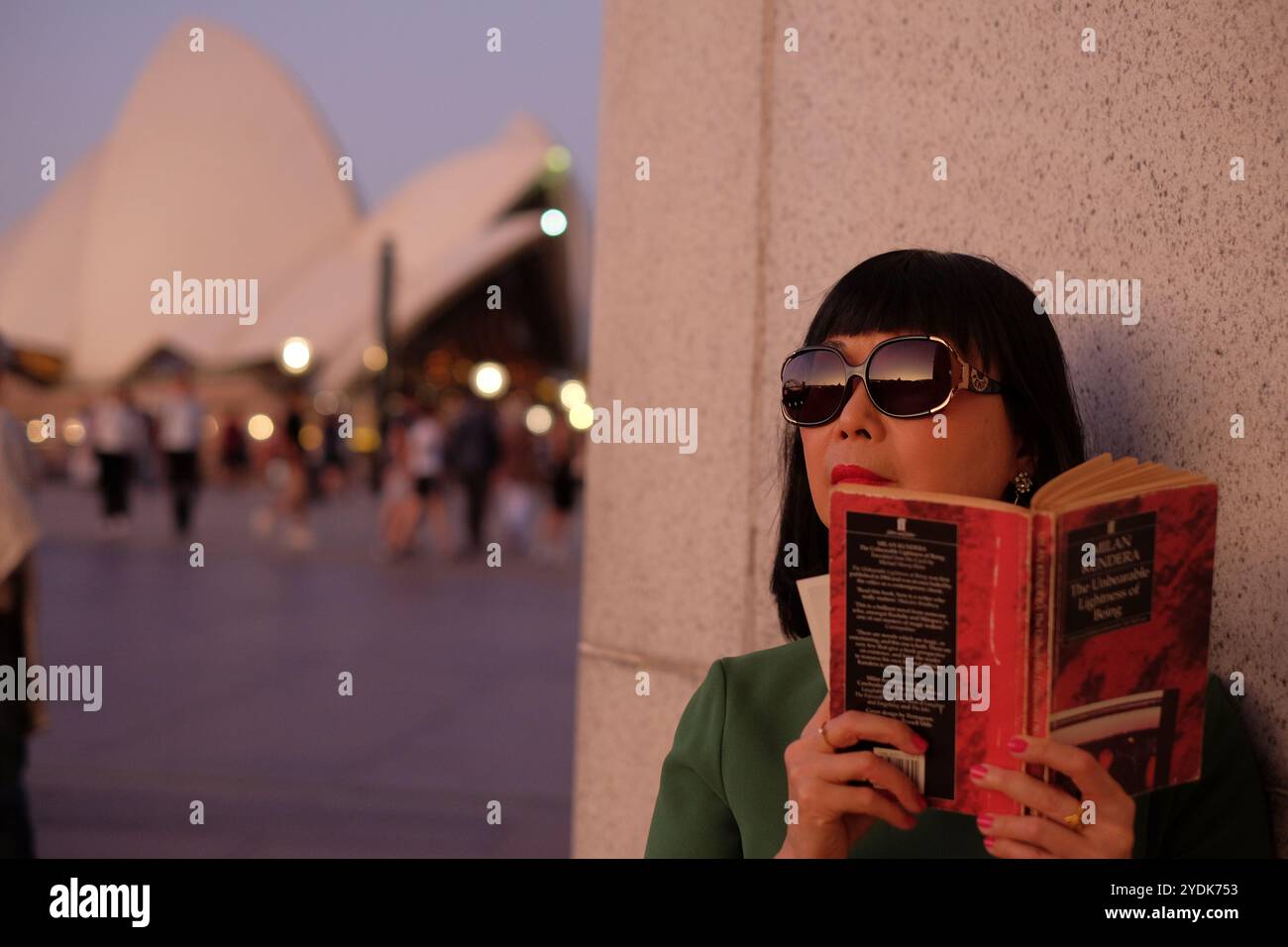 Une femme avec un livre, l'Opéra de Sydney au crépuscule avec des gens marchant dans le parvis, les voiles dans la lumière douce Banque D'Images