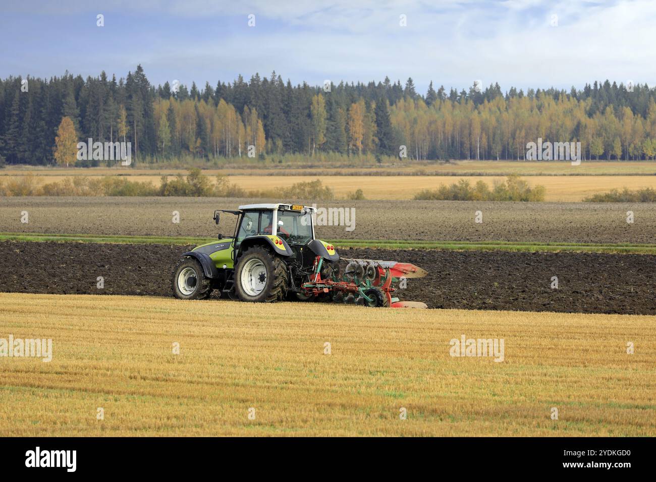 Les agriculteurs cultivent le champ avec un tracteur vert Valtra et labourent le matin ensoleillé de l'automne dans le sud de la Finlande. Jokioinen, Finlande. 2 octobre 2020 Banque D'Images