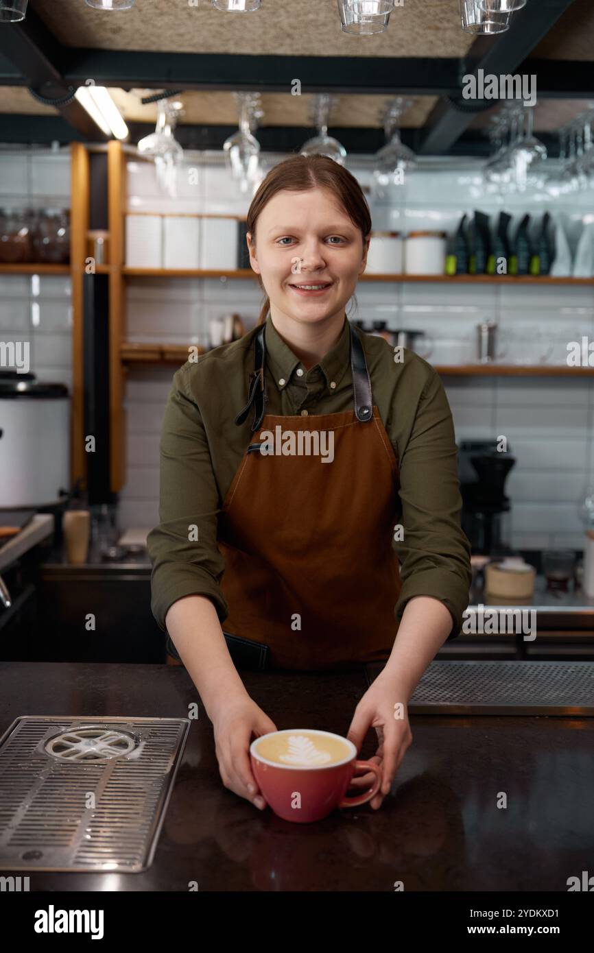 Portrait du barista au service d'un client qui donne un cappuccino ou un latte fraîchement préparé Banque D'Images