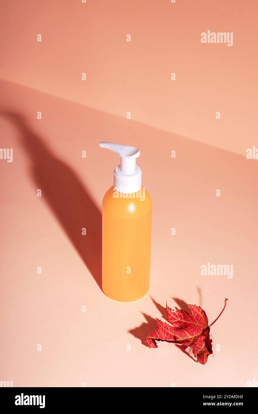 Bouteille cosmétique jaune et feuille d'automne rouge sur fond neutre avec ombre nette. Concept cosmétique naturel. Maquette. Banque D'Images