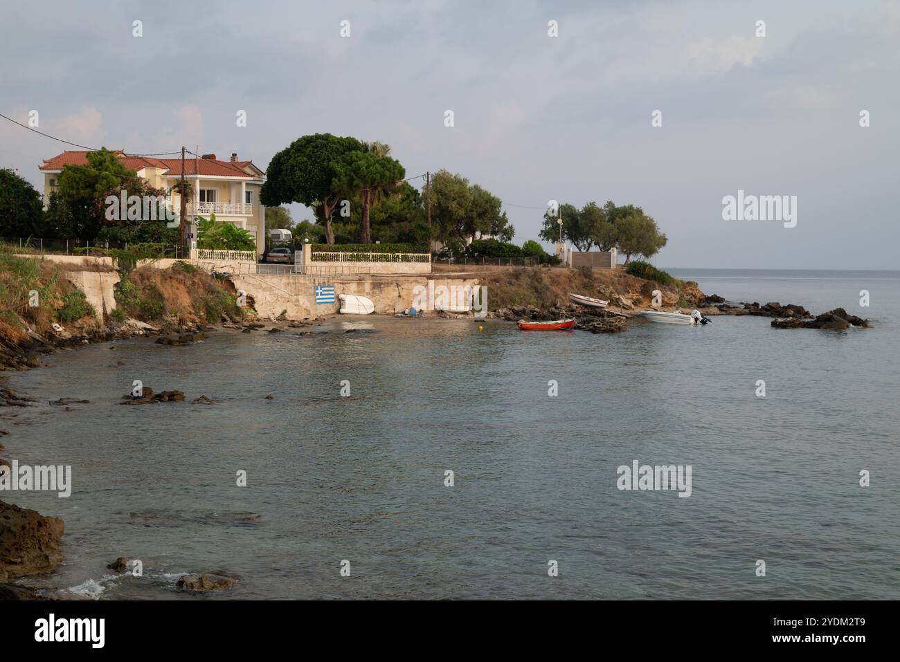 Maison sur le bord de mer entoure par des pins maritimes à proximité d'une jetée avec de petits bateaux amarrés et trois autres tractés hors de l'eau Banque D'Images