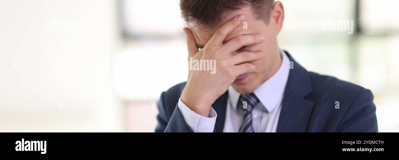 L'homme dépressif en costume habillé couvre le visage avec la paume dans le bureau Banque D'Images