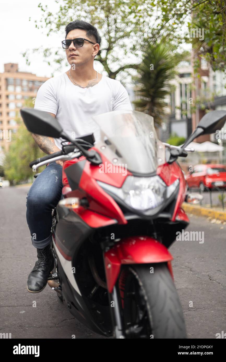 beau modèle masculin assis sur sa moto par une journée ensoleillée, style de vie, portrait de jeune personne latine portant des vêtements décontractés, moyens de transport Banque D'Images