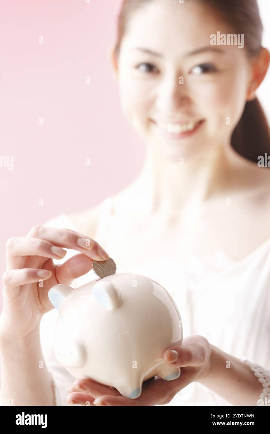 Woman putting money into piggy bank Banque D'Images