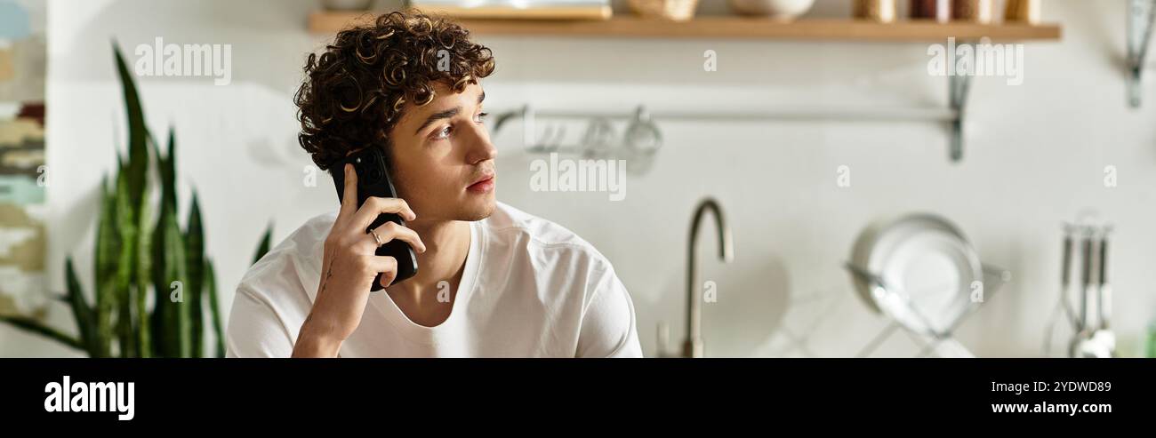 Un beau jeune homme converse au téléphone, entouré d'une cuisine élégante avec des plantes et un décor élégant. Banque D'Images