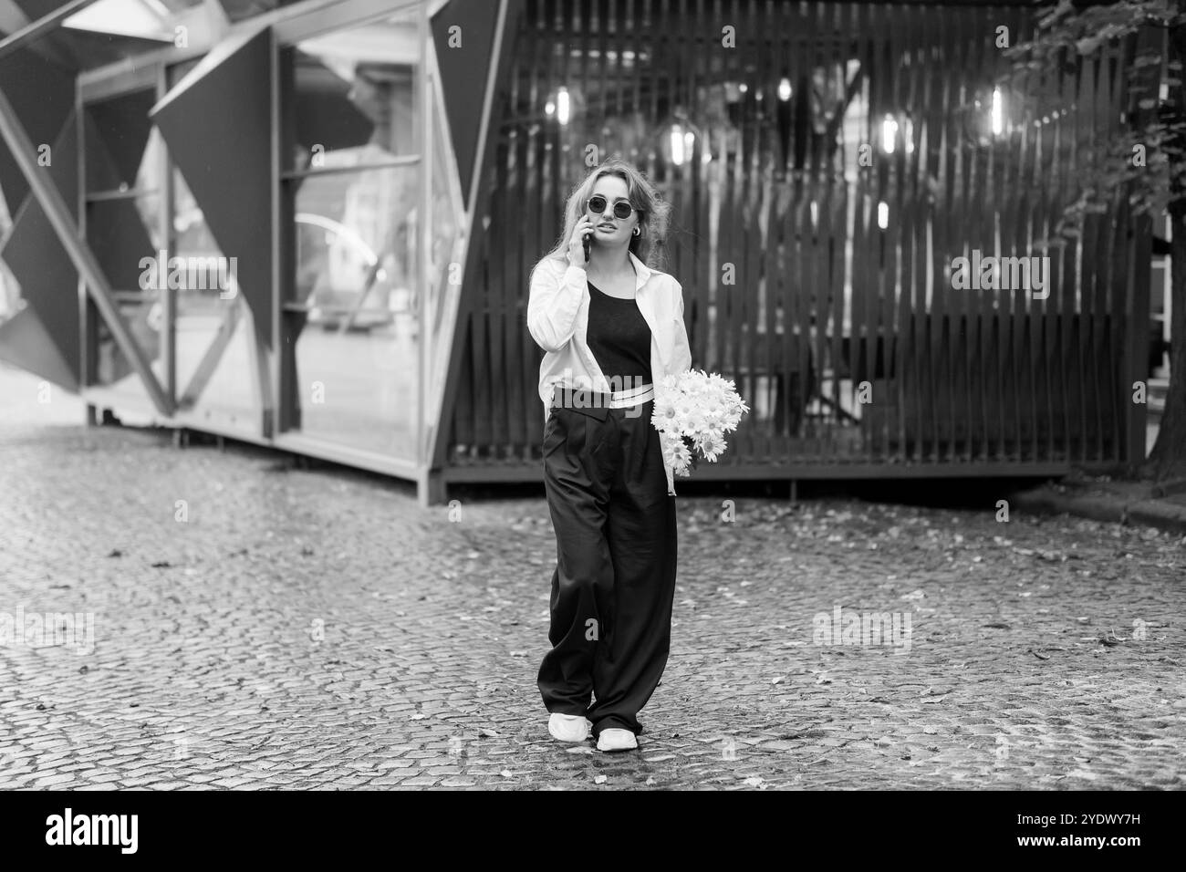 Femme élégante en noir et blanc mode se promenant avec des fleurs dans un cadre urbain. Banque D'Images