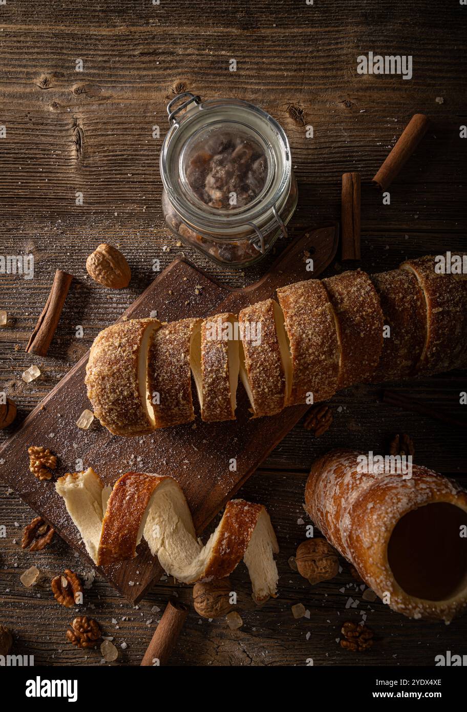 Gâteau traditionnel hongrois à la cheminée, un gâteau sucré à la broche, tranché et présenté sur une planche de bois rustique, garni de noix, de cannelle et de bonbons à la roche Banque D'Images