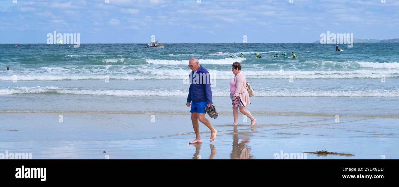 Une image panoramique d'un couyple de visiteurs de vacanciers matures marchant pieds nus le long du rivage sur Towan Beach sur la côte de Newquay à Cornwal Banque D'Images Une image panoramique d'un couyple de visiteurs de vacanciers matures marchant pieds nus le long du rivage sur Towan Beach sur la côte de Newquay à Cornwal Banque D'Images