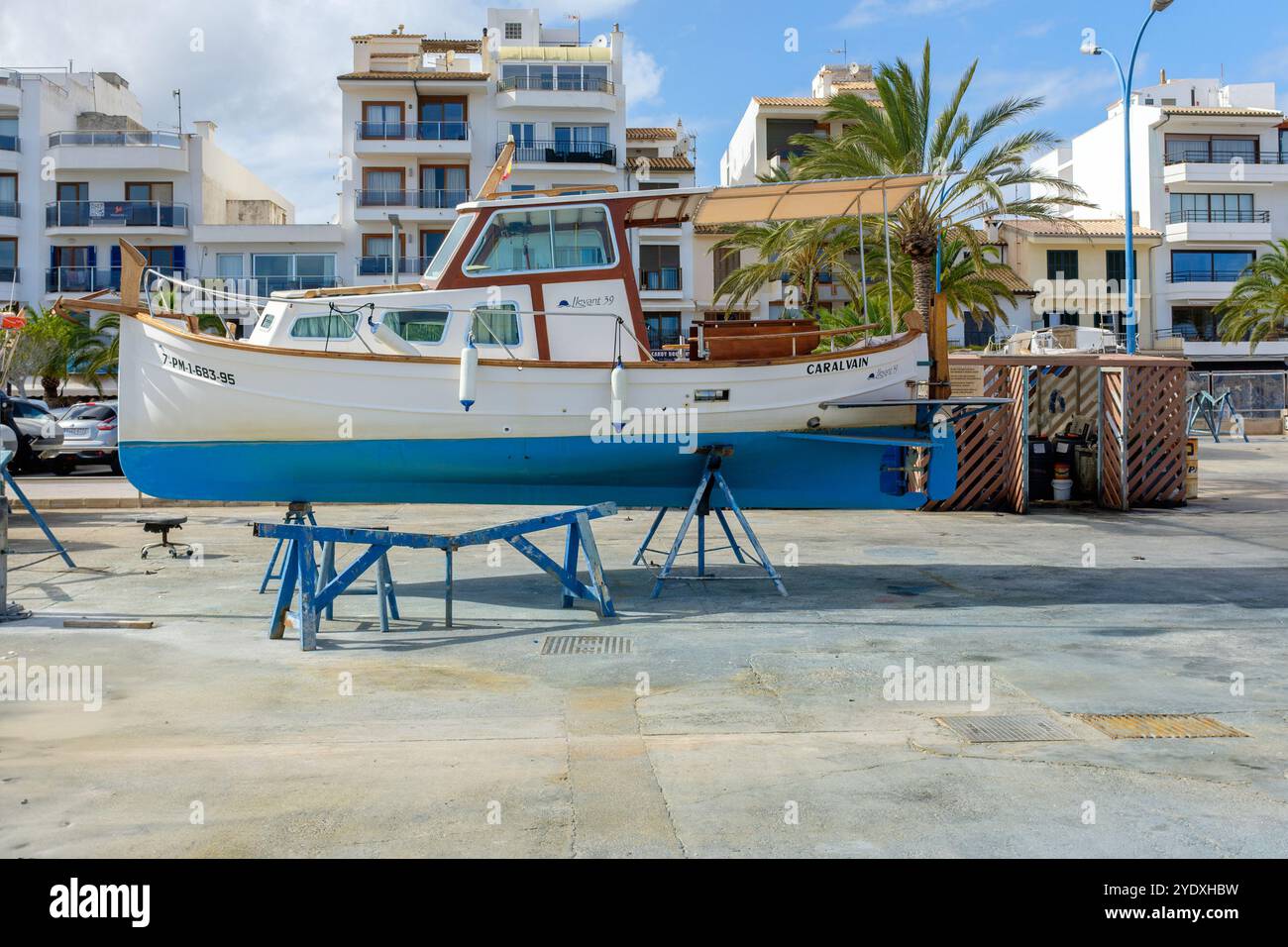 Un petit bateau bleu et blanc assis sur des supports ayant été soulevé de l'eau dans un chantier naval à Puerto Pollensa sur l'île espagnole de Majorque Banque D'Images
