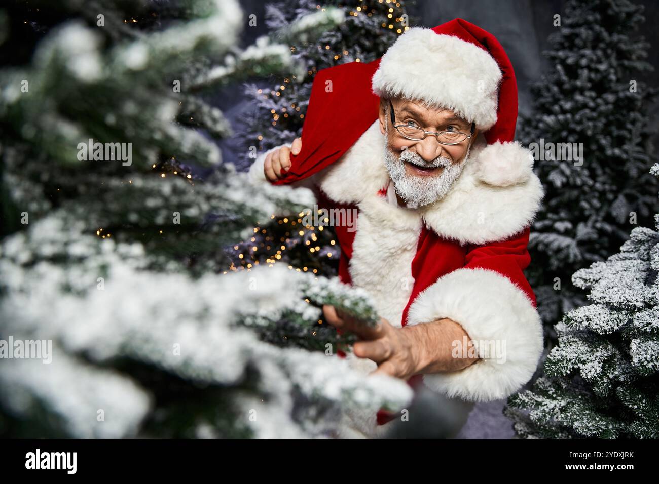 Un personnage festif en rouge et blanc s'étend au milieu des arbres de Noël enneigés, répandant la joie. Banque D'Images