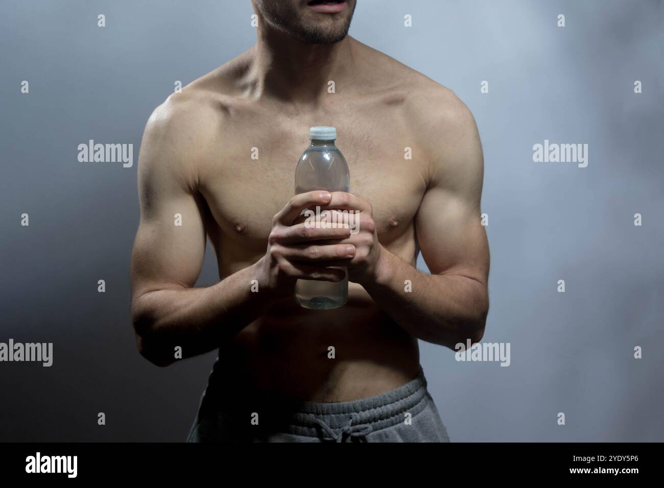 Un jeune corps masculin avec des abdominaux et une poitrine bien définis. Mannequin tenant une bouteille d'eau, avec torse torse torse nu. Concept de soins du corps, santé masculine, fitness, Banque D'Images