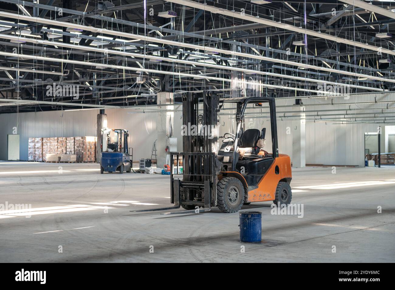 Grand intérieur d'entrepôt non fini avec chariots élévateurs, câblage exposé et matériaux de construction dispersés, mettant en évidence une rénovation industrielle active Banque D'Images