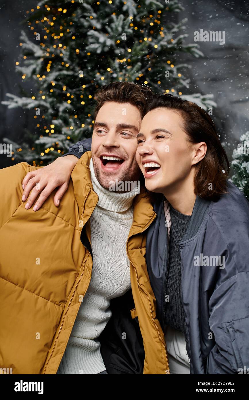 Un couple heureux embrasse, portant des vestes douillettes, entouré d'arbres couverts de neige, célébrant l'esprit de Noël. Banque D'Images