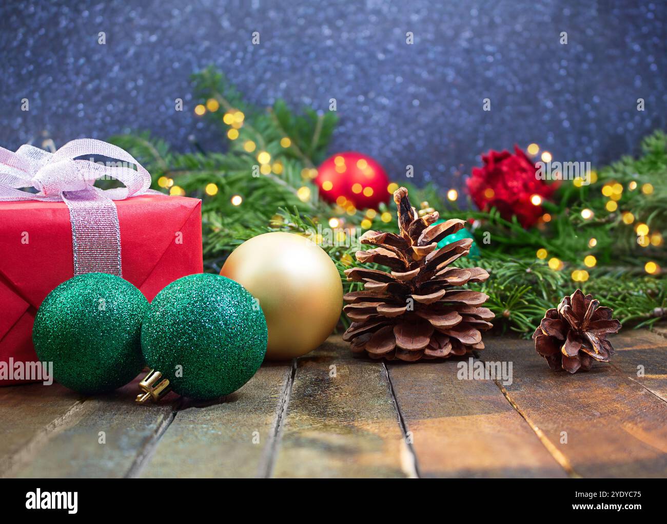 Boîte cadeau rouge avec arc, boules de paillettes, pommes de pin sur fond en bois, lumières floues sur le dos. Noël, nouvel an, vacances. Copier l'espace Banque D'Images