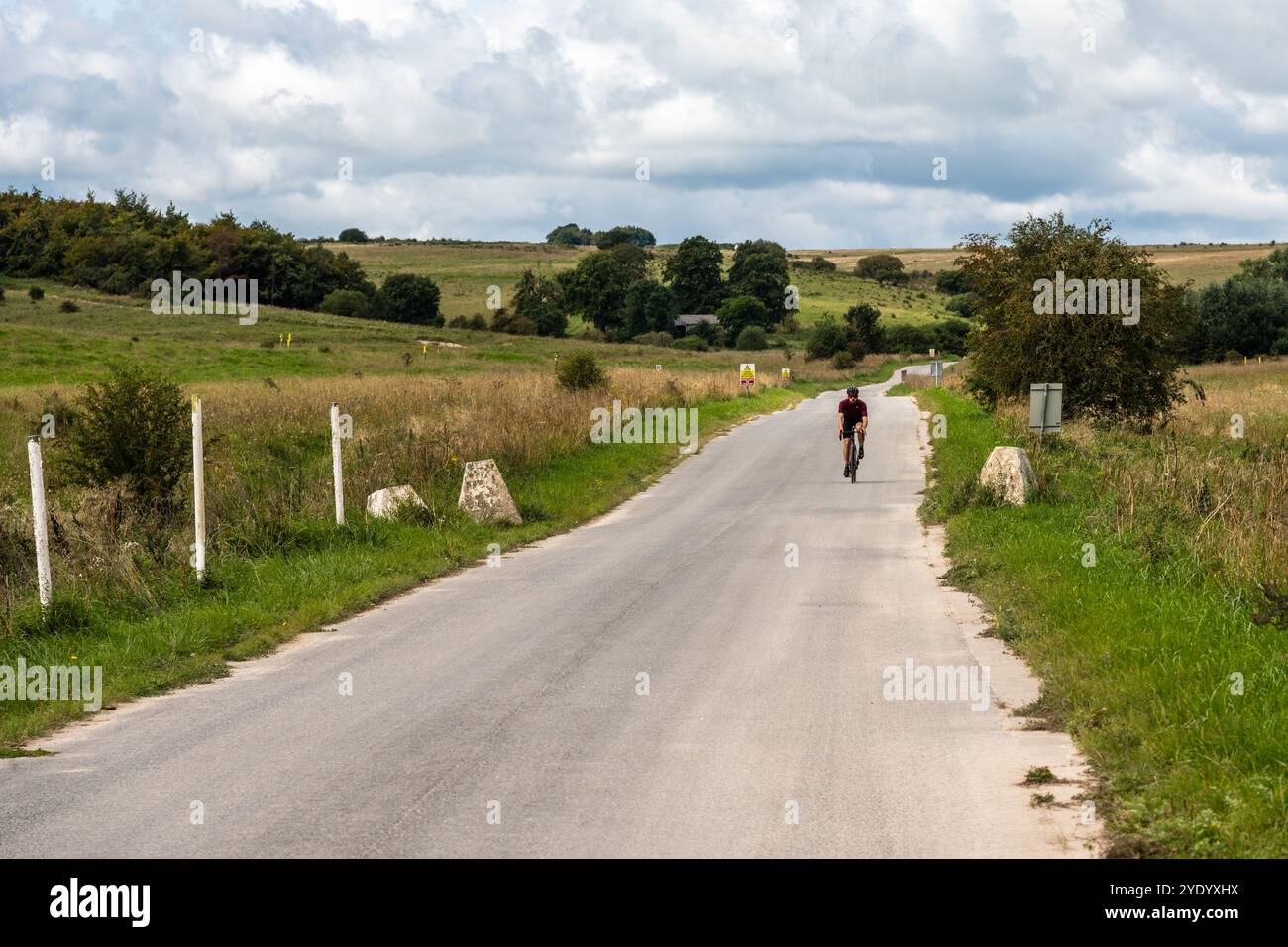 Un cycliste passe devant des panneaux d'avertissement sur une route traversant les Imber Ranges, la zone d'entraînement de l'armée britannique sur la plaine de Salisbury dans le Wiltshire, en Angleterre. Banque D'Images