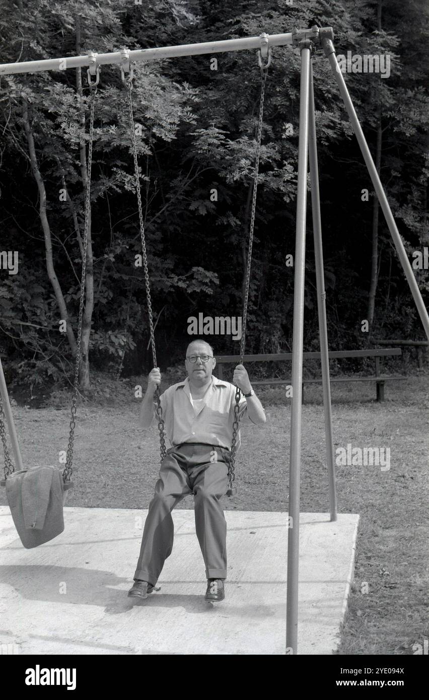 années 1950, historique, un homme mûr assis dehors sur une balançoire traditionnelle en bois de parc à mailles. Banque D'Images