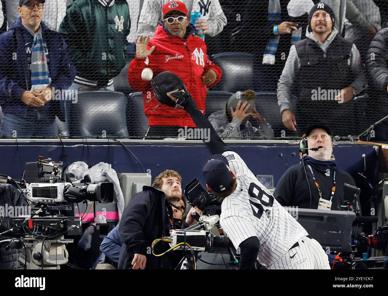 New York, États-Unis. 28 octobre 2024. Anthony Rizzo, premier joueur des New York Yankees, atteint mais ne peut pas attraper une balle malheureuse des Los Angeles Dodgers Mookie Betts comme le réalisateur Spike Lee regarde depuis la première ligne de la troisième manche du troisième match de la série mondiale MLB au Yankee Stadium de New York le lundi 28 octobre 2024. Photo de John Angelillo/UPI crédit : UPI/Alamy Live News Banque D'Images