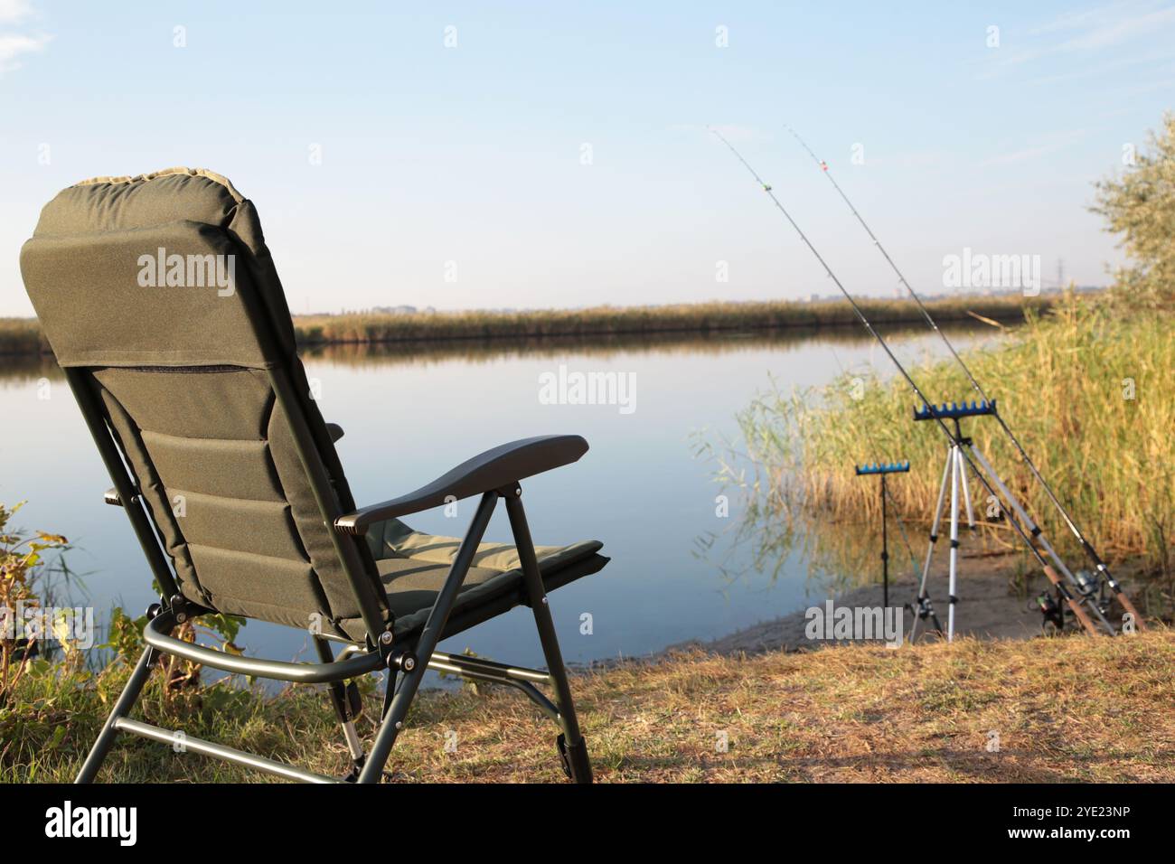 Chaise de pêcheur et cannes à pêche en arrière-plan sur la rivière au lever du soleil, matin brumeux. Concept de pêche. Beau lever de soleil - paysage du matin. Banque D'Images