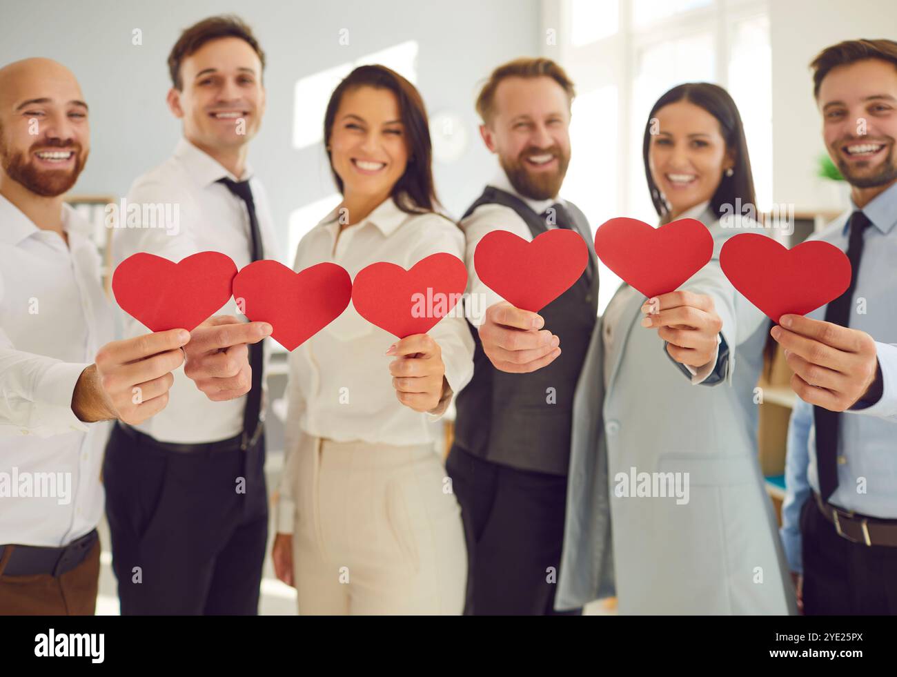 Équipe d'entreprises diversifiées debout dans le bureau, souriant et tenant des cœurs de papier rouge Banque D'Images