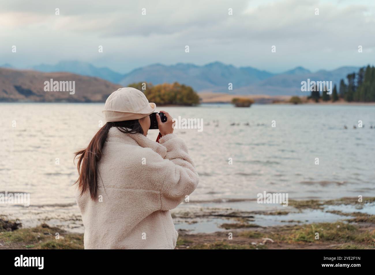 Vue arrière de la touriste profitant et prenant une photo avec un appareil photo compact sur le lac Tekapo en automne à la Nouvelle-Zélande Banque D'Images