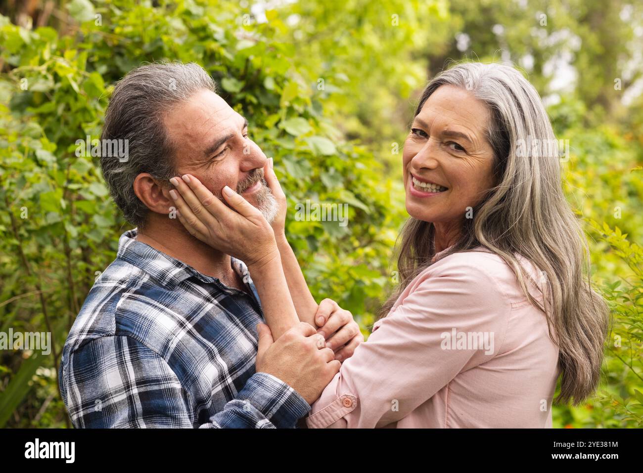 Couple mature souriant profitant d'un moment tendre ensemble dans un jardin luxuriant, à l'extérieur Banque D'Images
