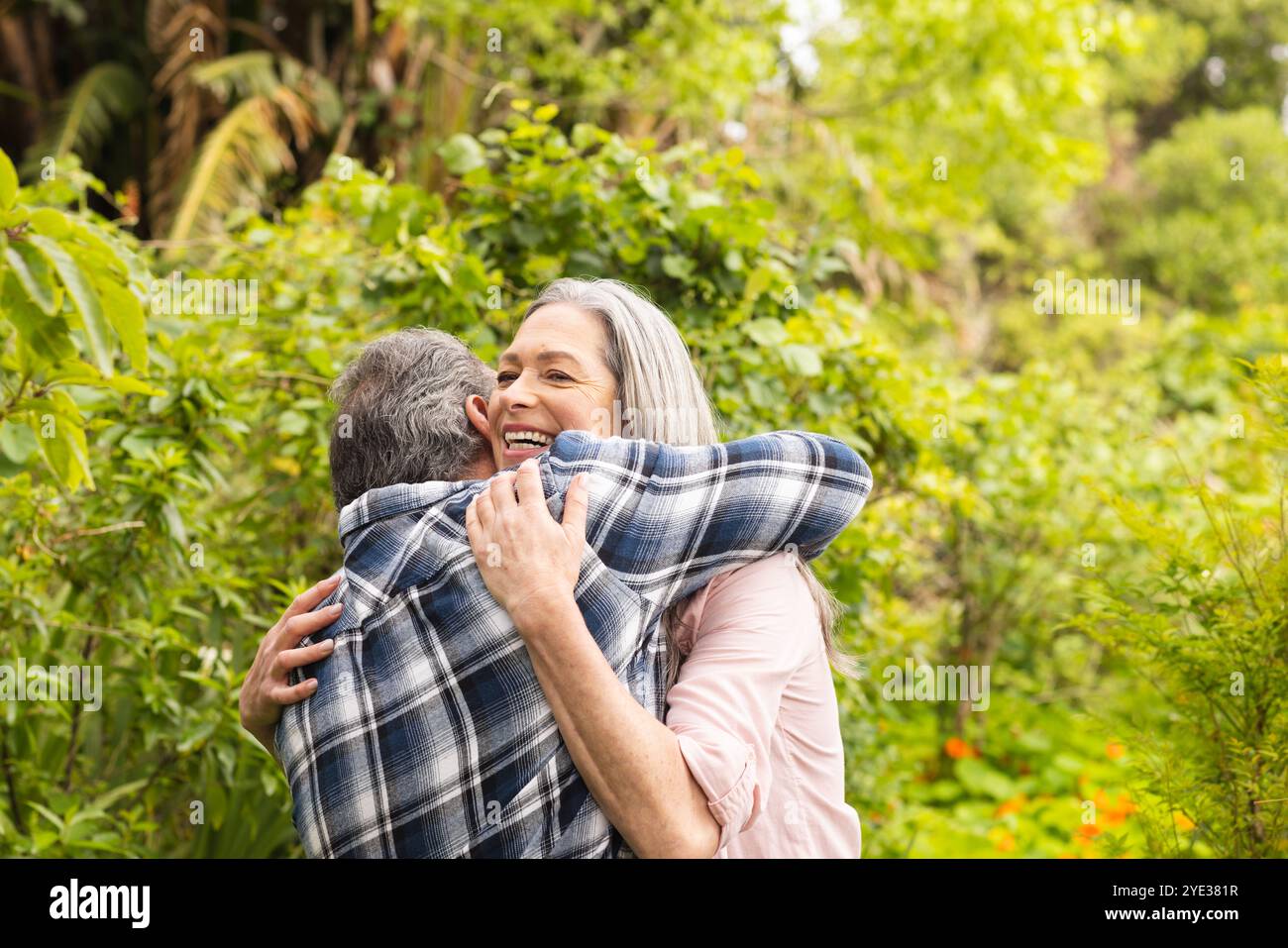 Couple d'âge mûr embrassant joyeusement dans un jardin luxuriant, célébrant la convivialité en plein air Banque D'Images
