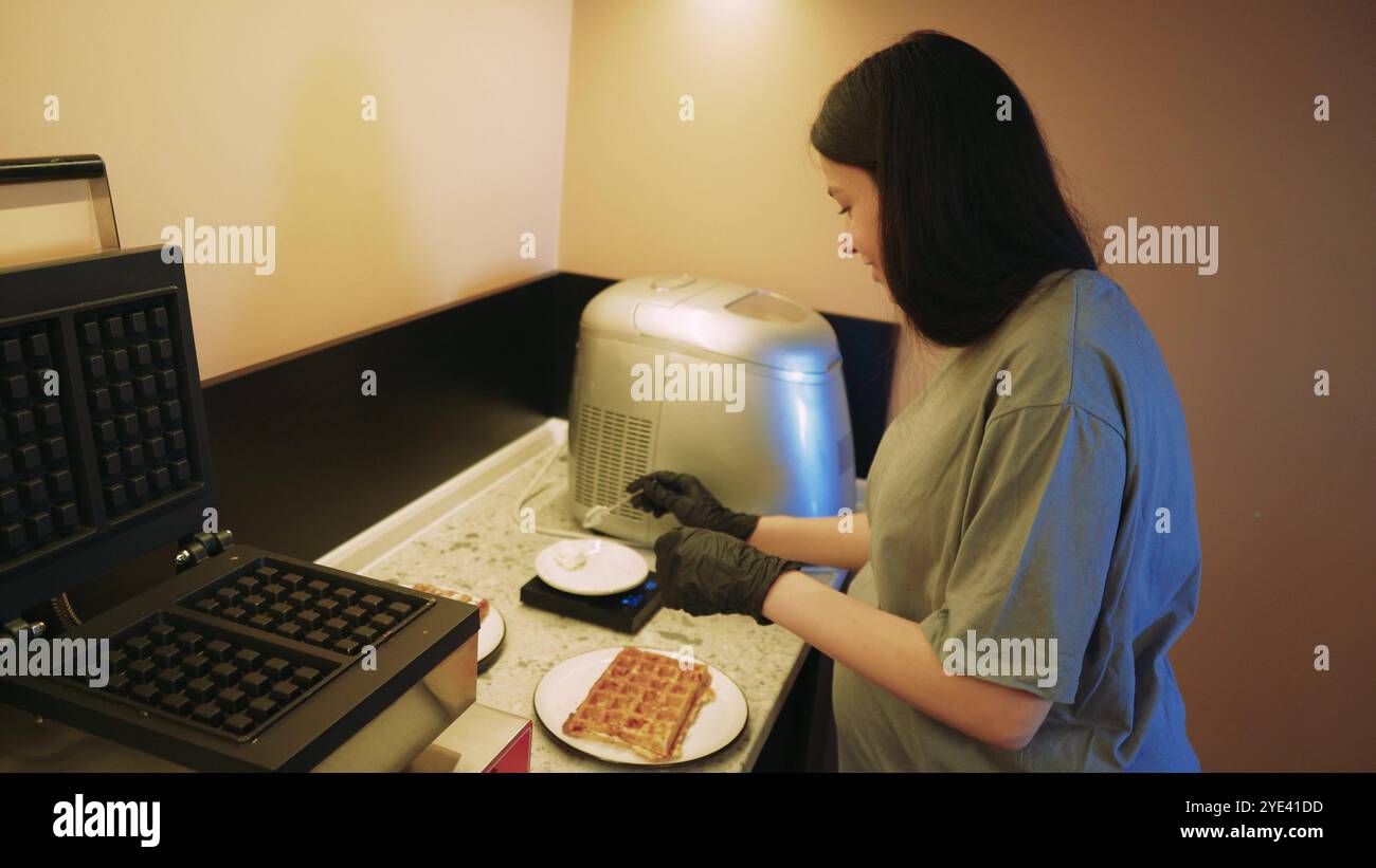 Il y a une gaufre préparée sur une assiette et un jeune cuisinier termine la préparation du plat fini. La cuisine d'un petit café confortable. Banque D'Images