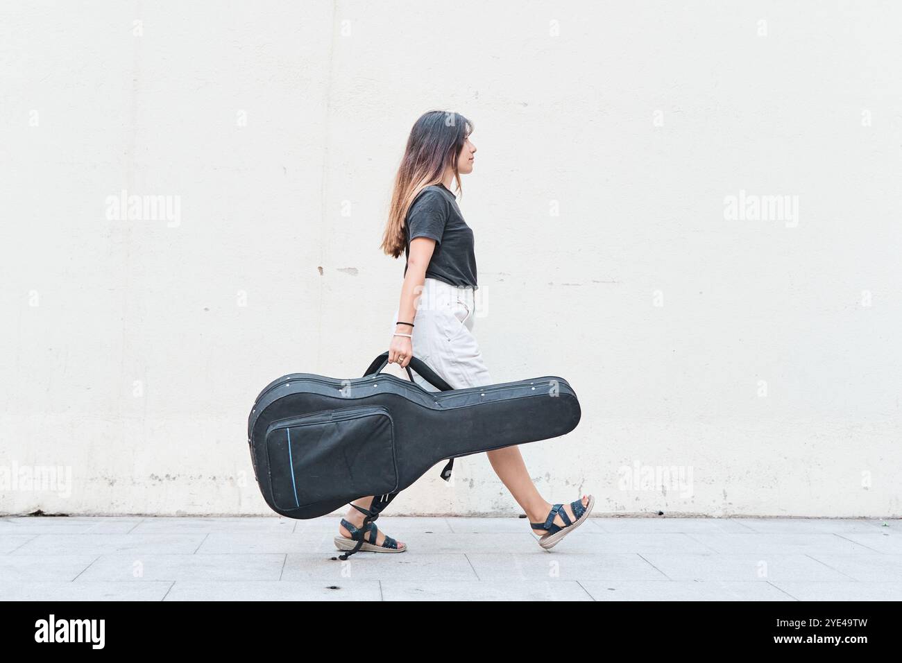 Femme caucasienne portant un étui de guitare sur le trottoir Banque D'Images